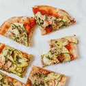 Sechs Pizzastücke mit Zucchini, Tomatensauce und Kräutern auf weißem Hintergrund